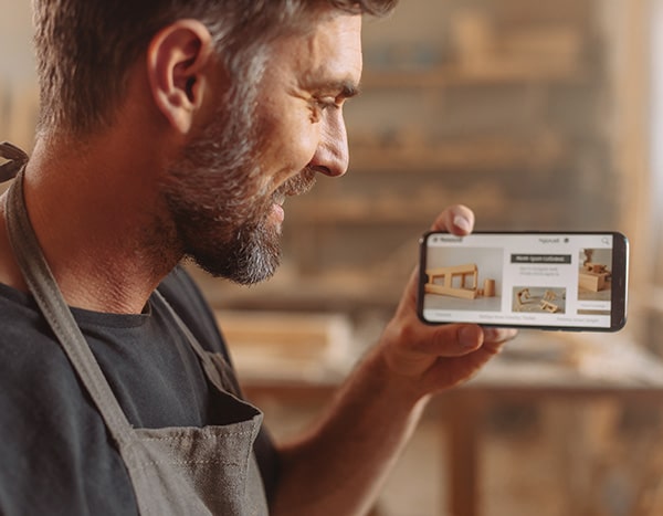 Handwerker in Arbeitsschürze betrachtet auf dem Smartphone lächelnd die mobile Ansicht seiner neuen Webseite